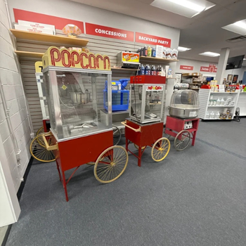 Three vintage-style concession carts with popcorn and cotton candy machines in a store aisle. Bright red base and glass cases showcase classic snacks. The atmosphere is nostalgic and inviting.