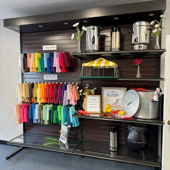 A display shelf features colorful napkins, silver beverage dispensers, and lemonade stand decor. Bright, organized, and inviting ambiance.