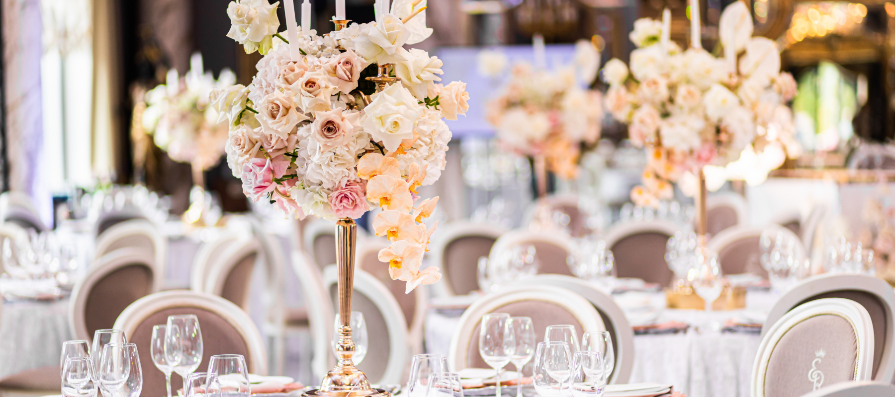 Elegant banquet hall with lavish floral centerpieces of white and pink roses on dining tables. The atmosphere is luxurious and festive.
